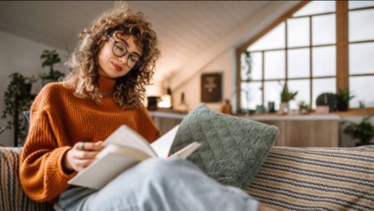 Persona utilizando una computadora para comprar libros online, con pilas de libros de fondo.