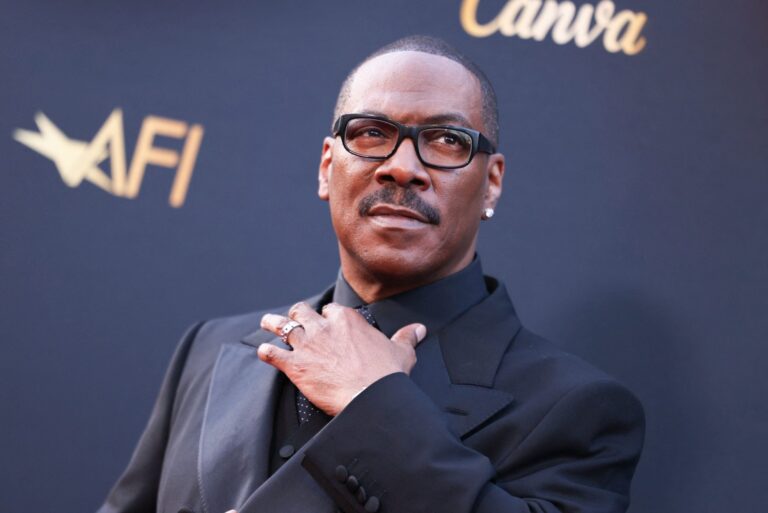 Eddie Murphy sonriendo mientras sostiene el premio a la trayectoria del AFI en el escenario.