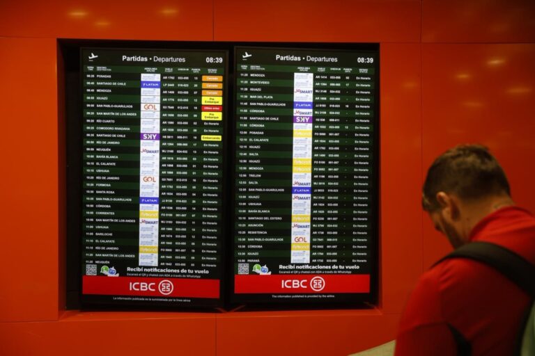 Pasajeros consultando pantallas de información de vuelos en un aeropuerto.